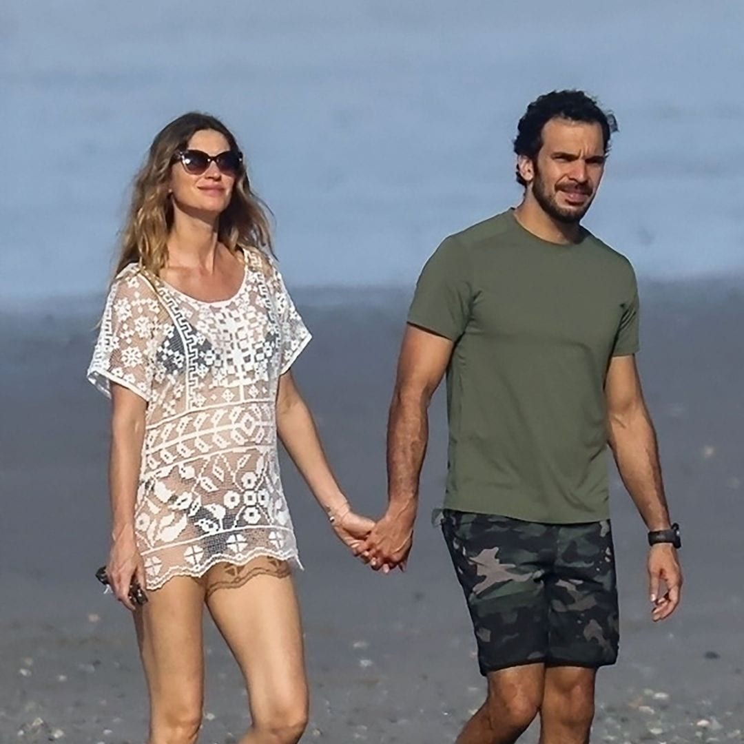 La pareja pasea junto a la orilla del mar. Para la ocasión, ella apostó por un bikini negro y un minivestido blanco de encaje y transparencias