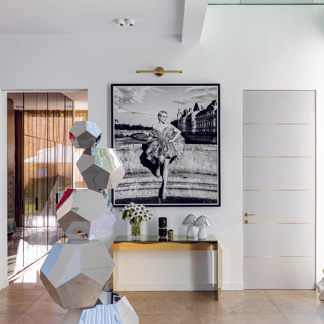 Sala moderna con arte en las paredes, mesas con flores y una escultura central.