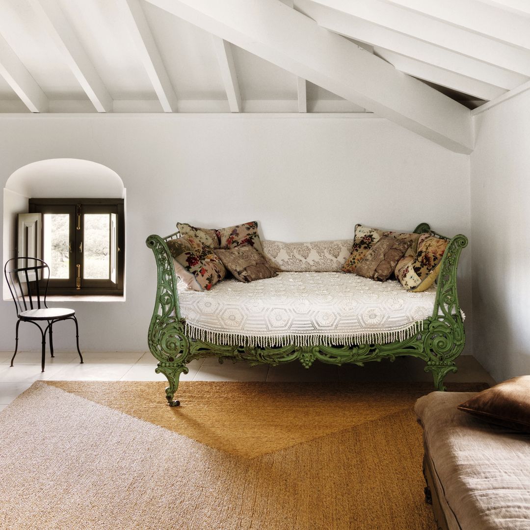 Habitación con sofá verde antiguo, varias almohadas, silla y ventana.