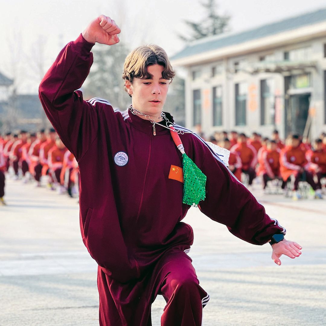 Simeón practicando artes marciales frente a grupo en uniforme rojo.