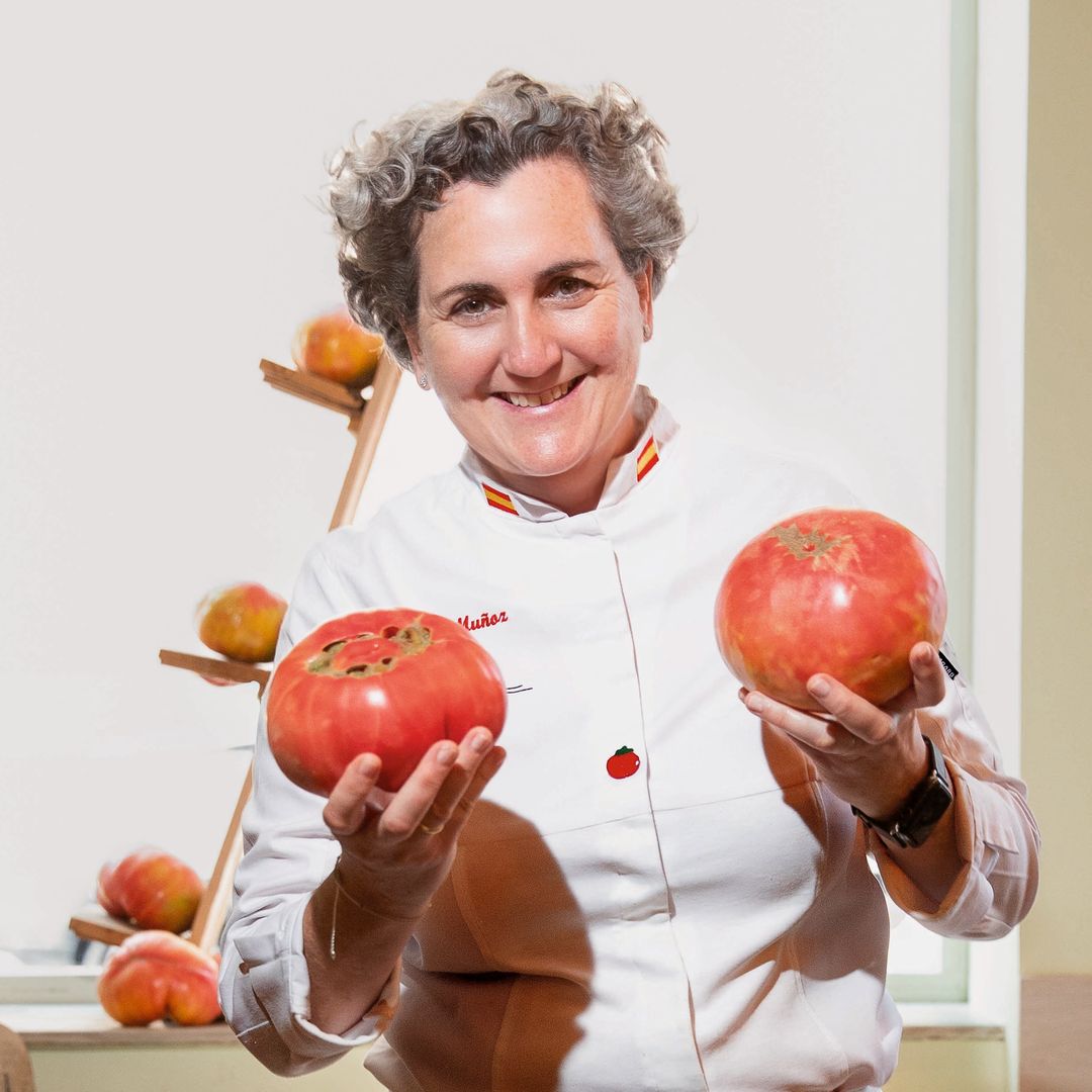 Pepa Muñoz con uniforme blanco sostiene dos manzanas rojas en una cocina.