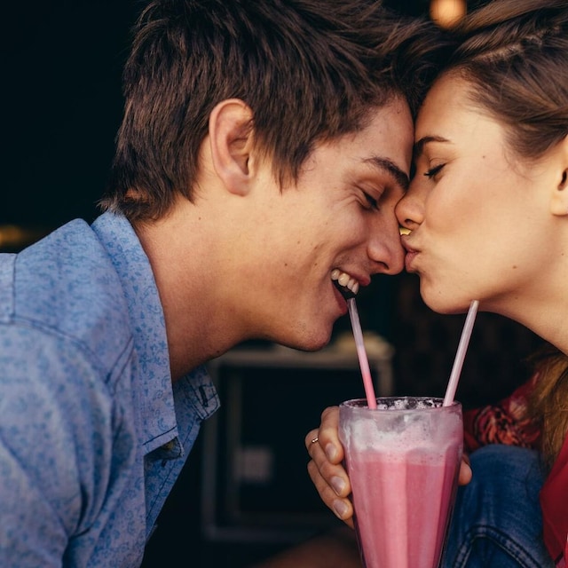 dos adolescentes d ndose un beso mientras beben un batido de fresa 