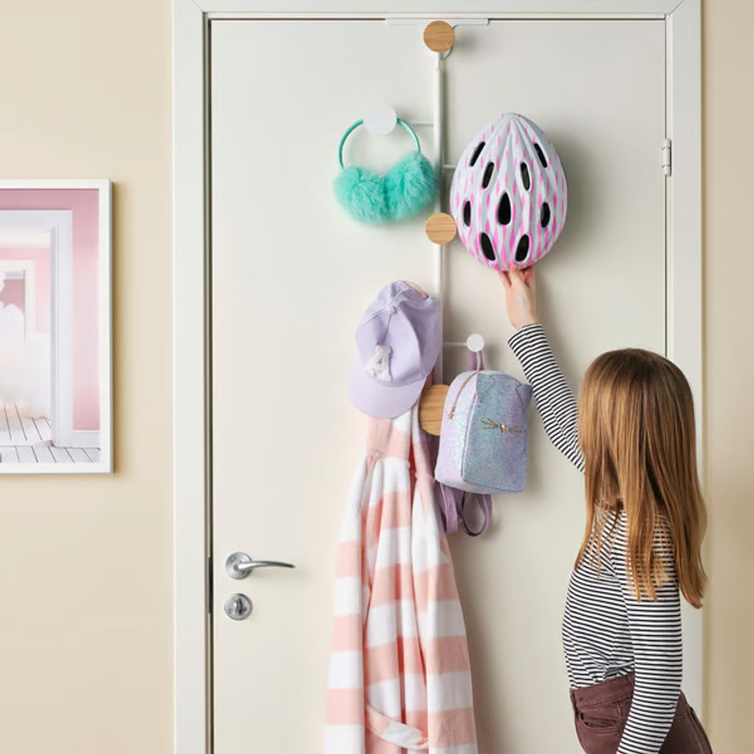 Niña colgando el casco de la bicicleta en el perchero por detrás de una puerta en IKEA.