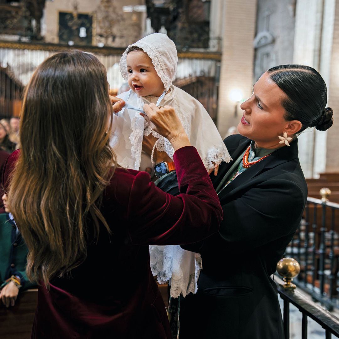 Lourdes ajusta la capota a Nicolás, al que sostiene su madrina, Paloma Rojas-Marcos