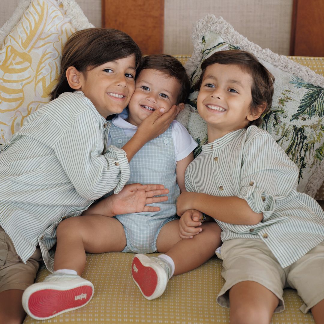 Tres niños sonrientes en un sofá, con un niño en medio abrazado por los otros dos.