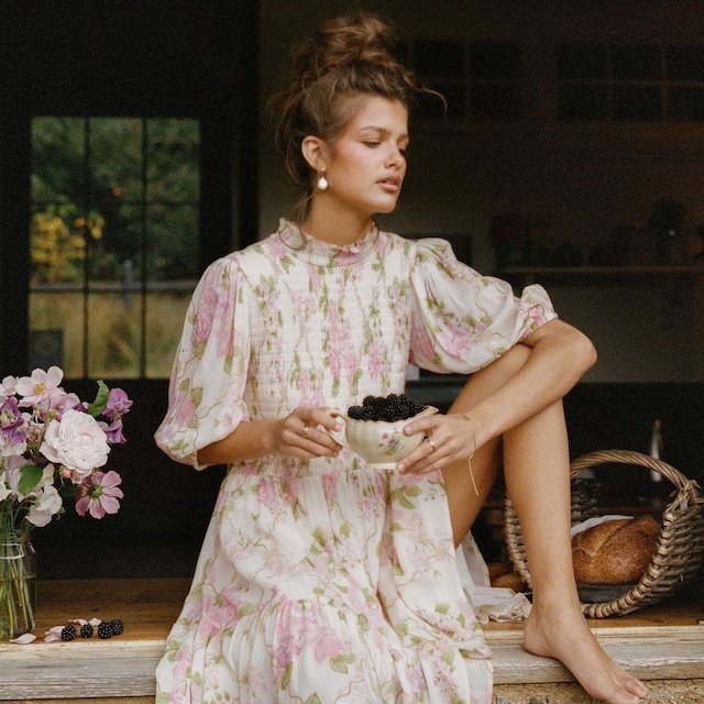 Mujer tomando moras en una ventana con vestido de flores y moño alto