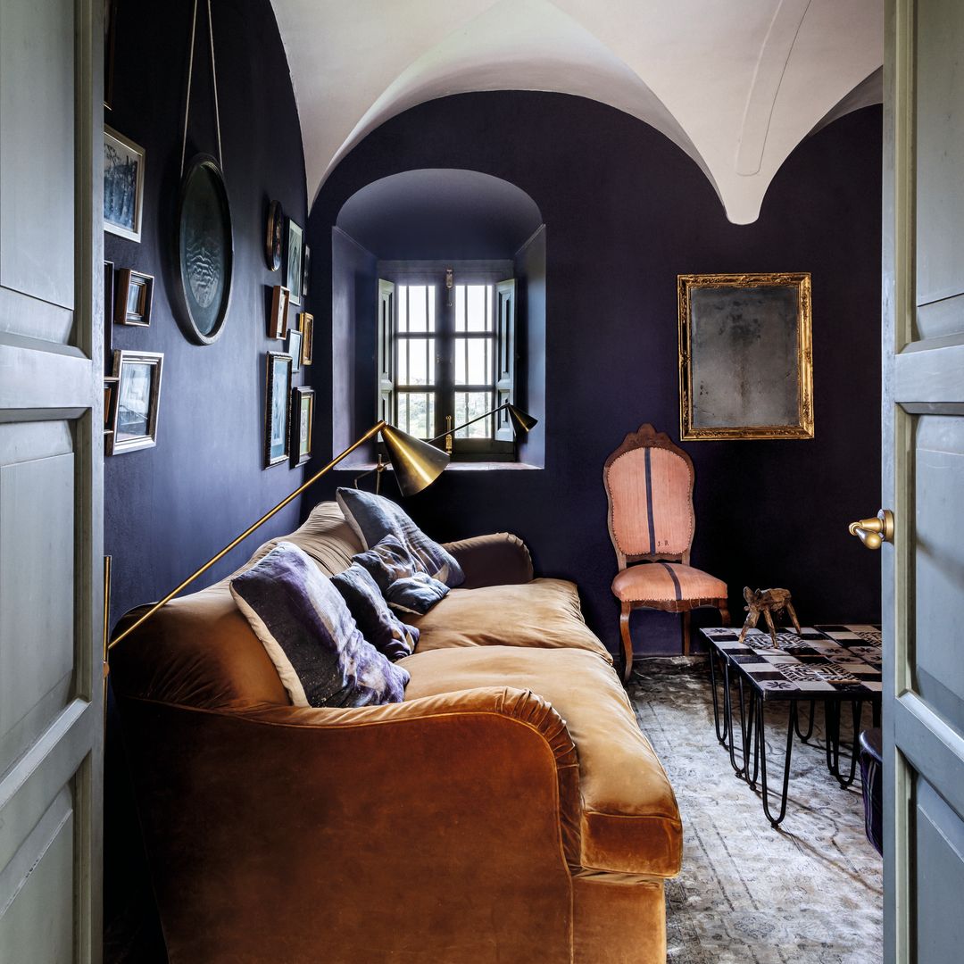 Sala con sofá marrón, silla rosa, y paredes azules con cuadros.