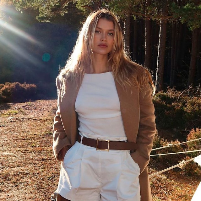 Plano medio de Chloe Lecareux con bermudas cortas blancas y abrigo marrón