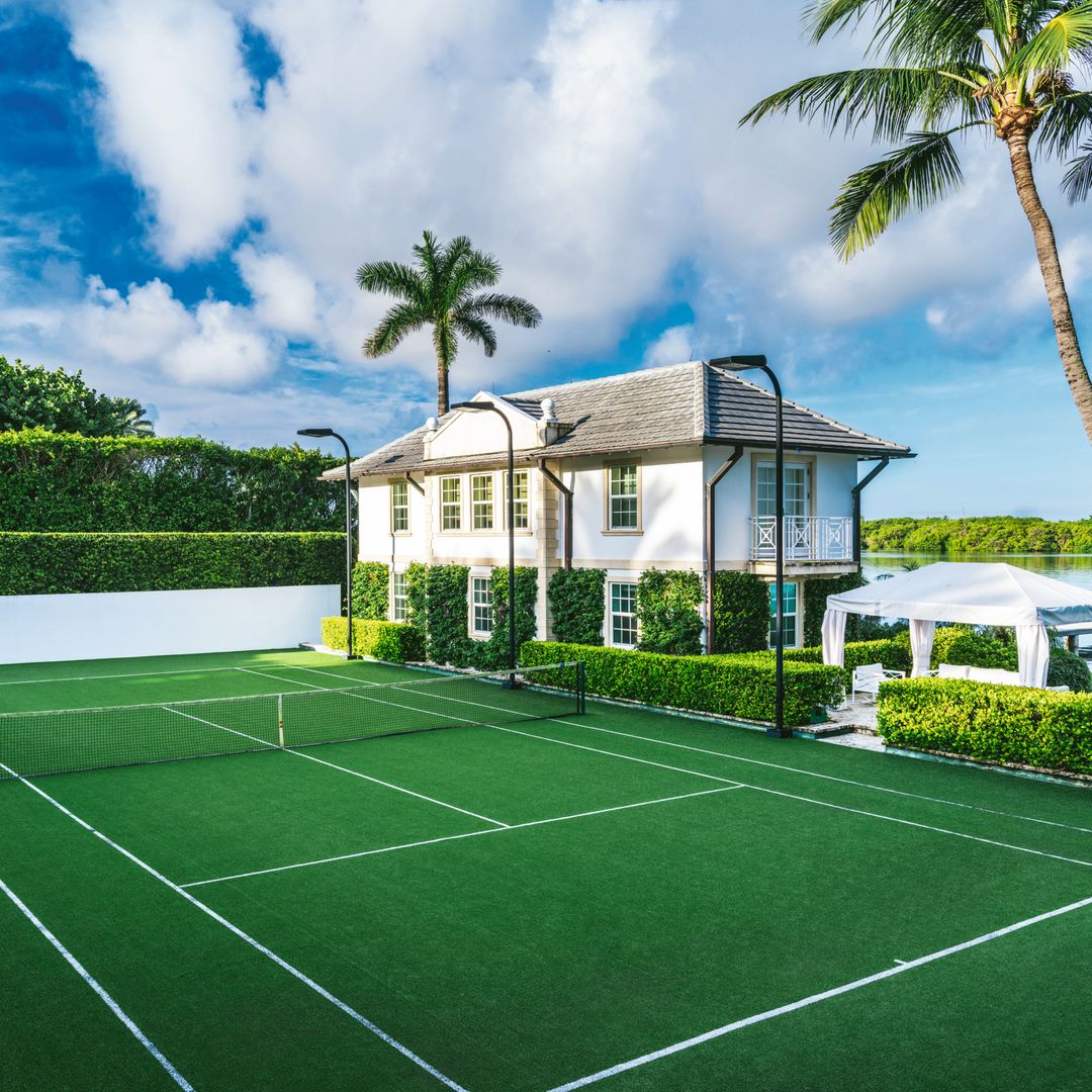 Cancha de tenis privada en un lujoso jardín, casa al fondo
