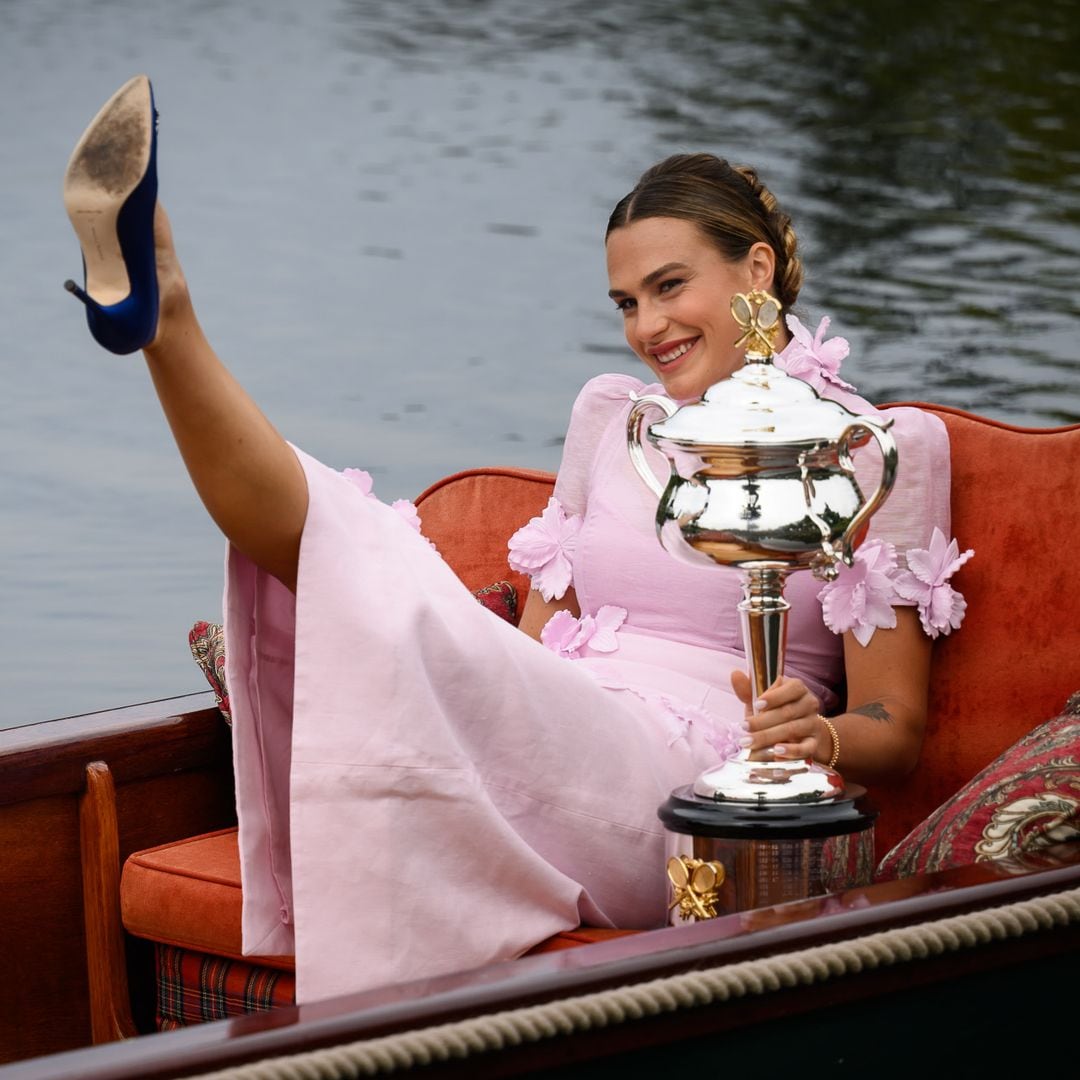 Aryna Sabalenka sonriendo en un bote, sosteniendo un trofeo y luciendo un vestido rosa.