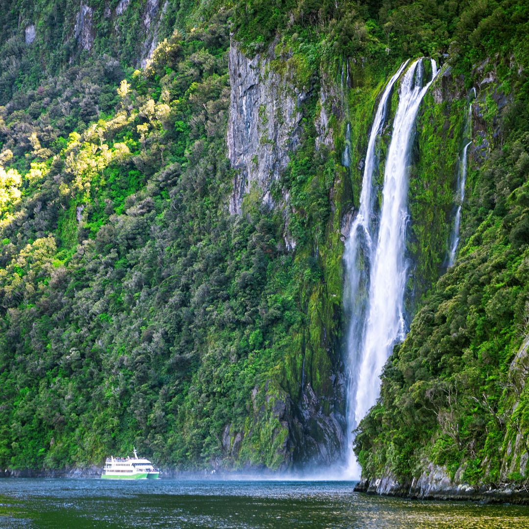 El barco turístico se aproxima a una cascada en el fiordo de Milford Sound, Nueva Zelanda.