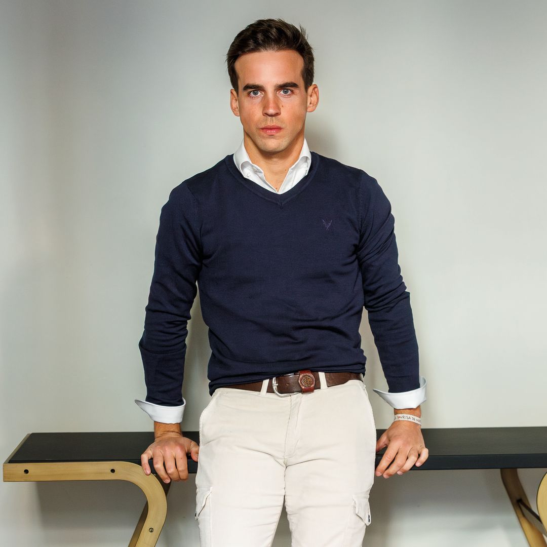 Gonzalo Caballero con cabello corto, camisa azul y pantalones beige, apoyado en una mesa.