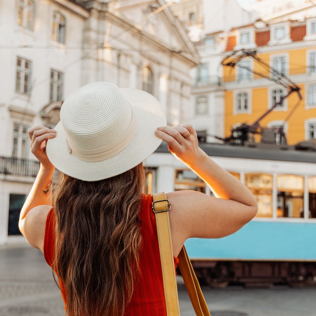 Chica joven con sombrero mirando cómo pasa un tranvía en Lisboa, en verano.