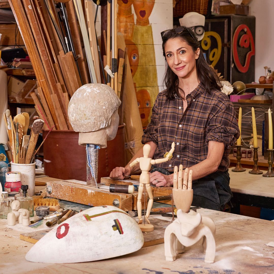 Claudia, en uno de los espacios de trabajo del taller, donde da forma a sus esculturas, rodeada de varias de sus coloridas obras pictóricas