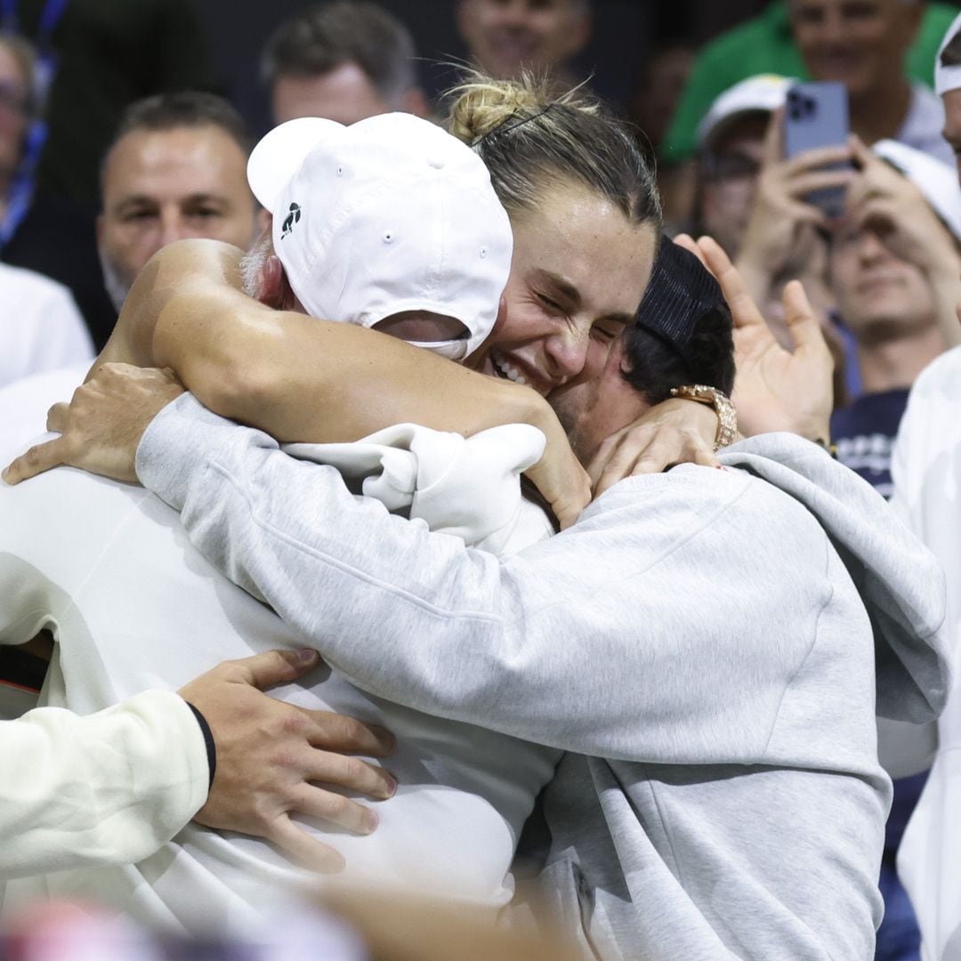 Aryna Sabalenka abrazada con dos personas, todos ríen y celebran en un estadio.