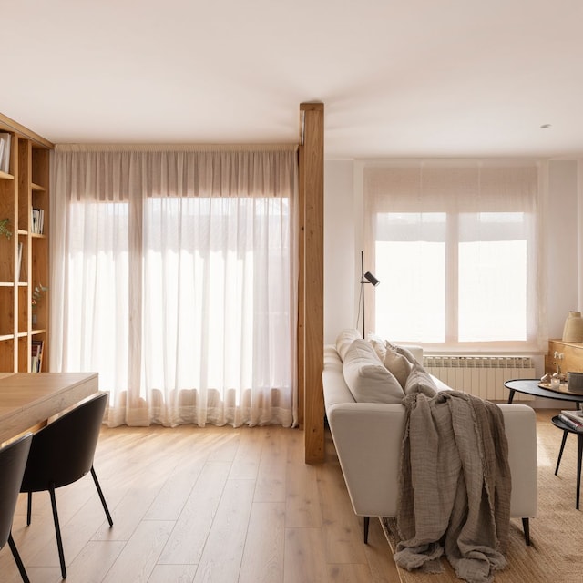 Salón comedor con sofá blanco, tabique de listones de madera, mesa de comedor y estantería de madera y cortinas claras