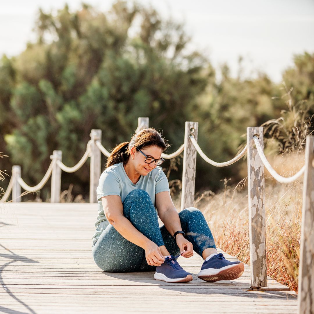 Mujer atándose los cordones en el paseo de madera de una playa preparada para caminar.