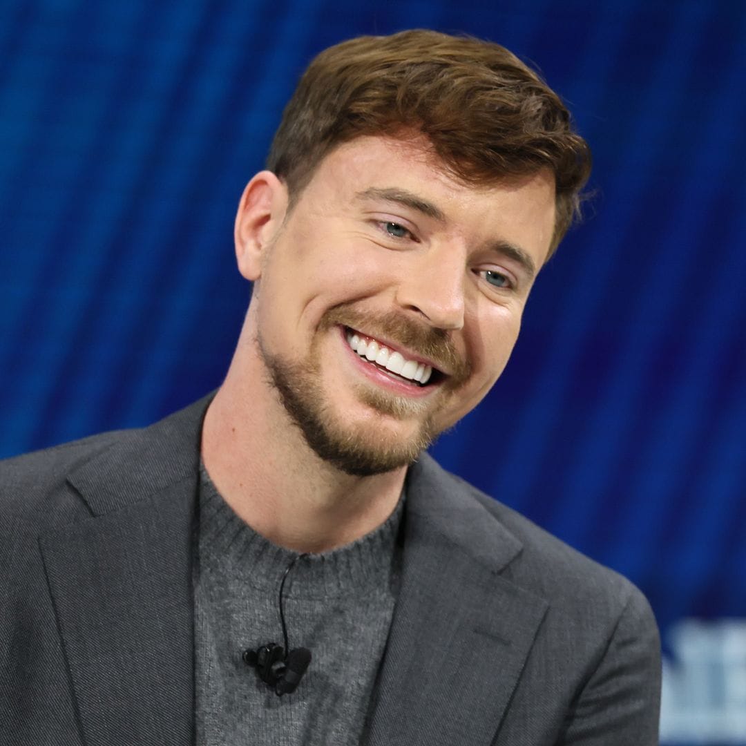 MrBeast sonriendo en un evento, vistiendo traje gris y camiseta gris.