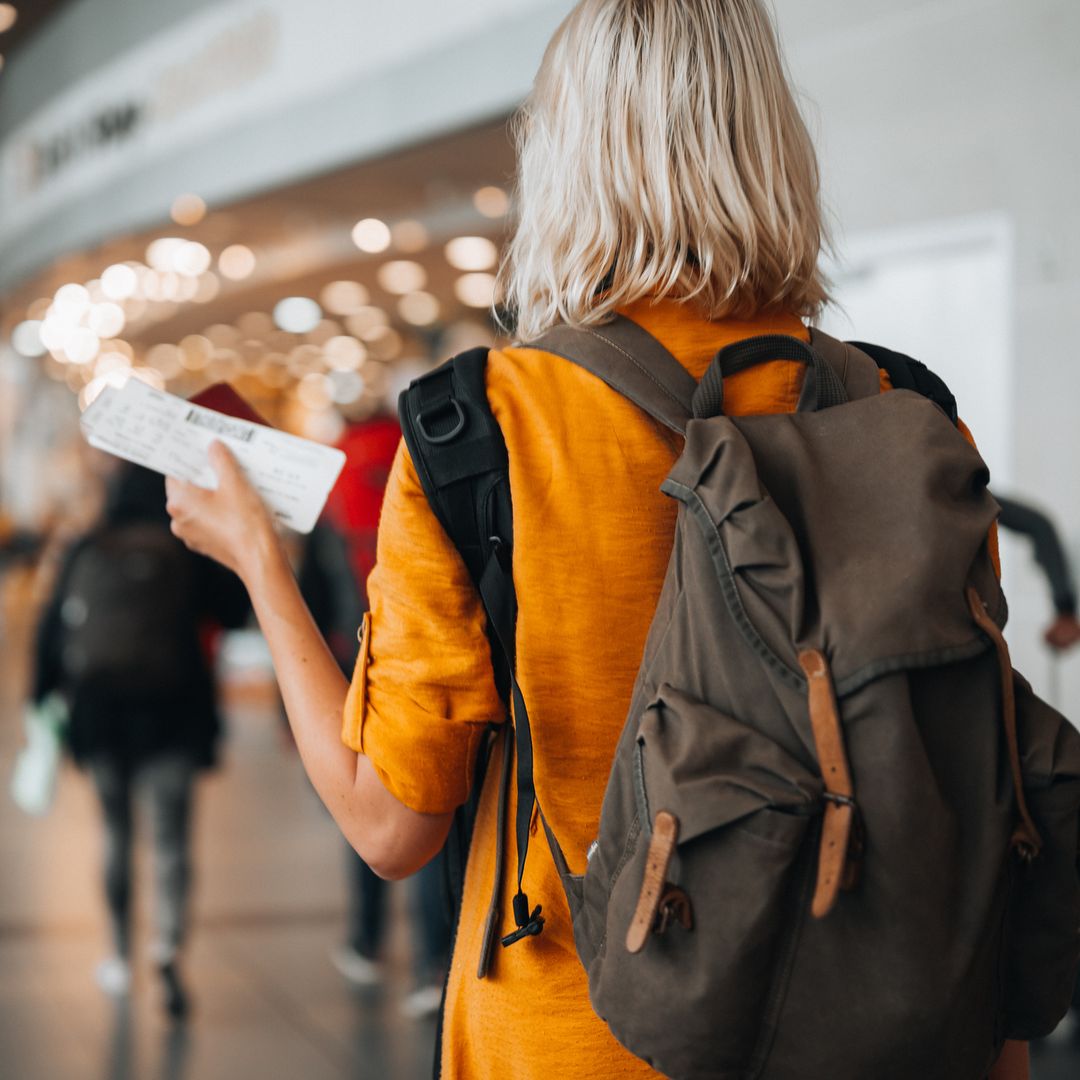 Mujer con los billetes de un avión en la mano durante un viaje, con mochila y de espaldas.