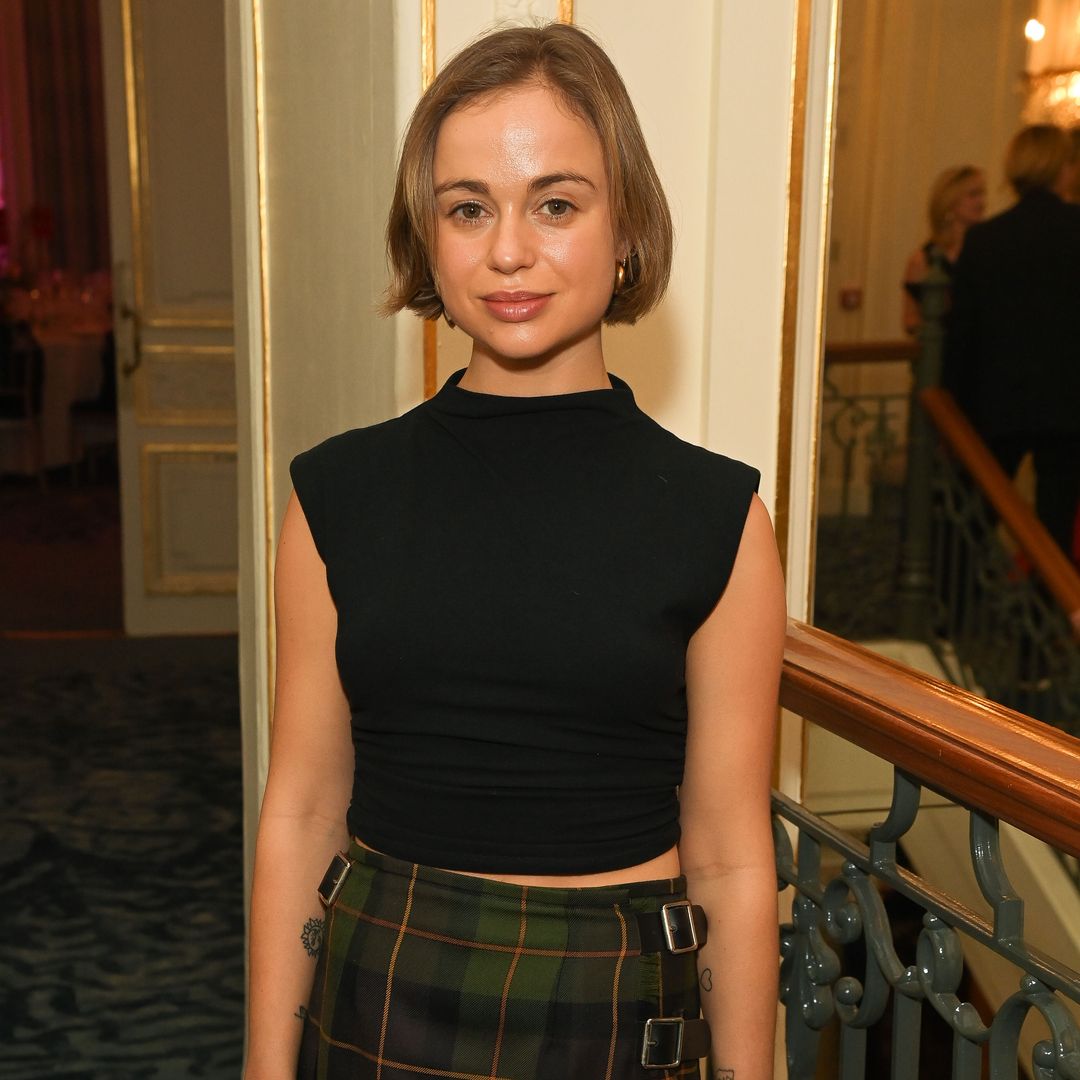 Plano medio de Amelia Windsor con top negro y falda escocesa midi