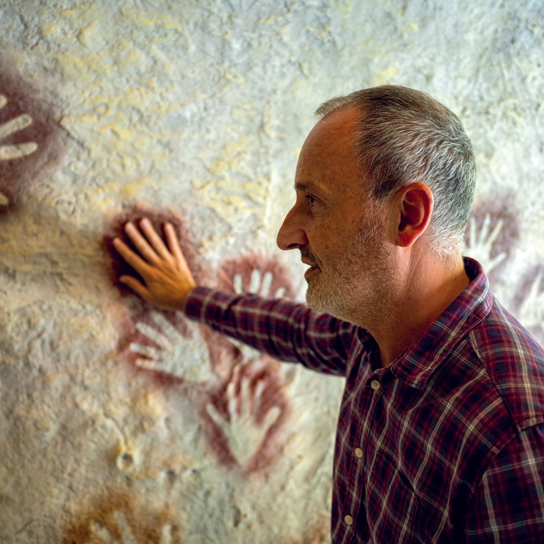 Eduardo Palacio-Pérez muestra el panel con las manos en negativo de la cueva El Castillo de Puente Viesgo.