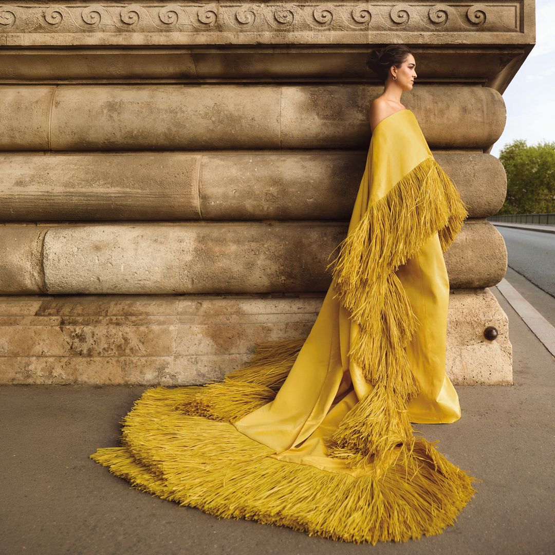 En un rincón de París, Bárbara Mirjan posa con vestido de corte sirena en color mostaza, con capa XL en el mismo tono, terminada en flecos al tono, de la colección de alta costura de Imane Ayissi, y joyas de Rabat