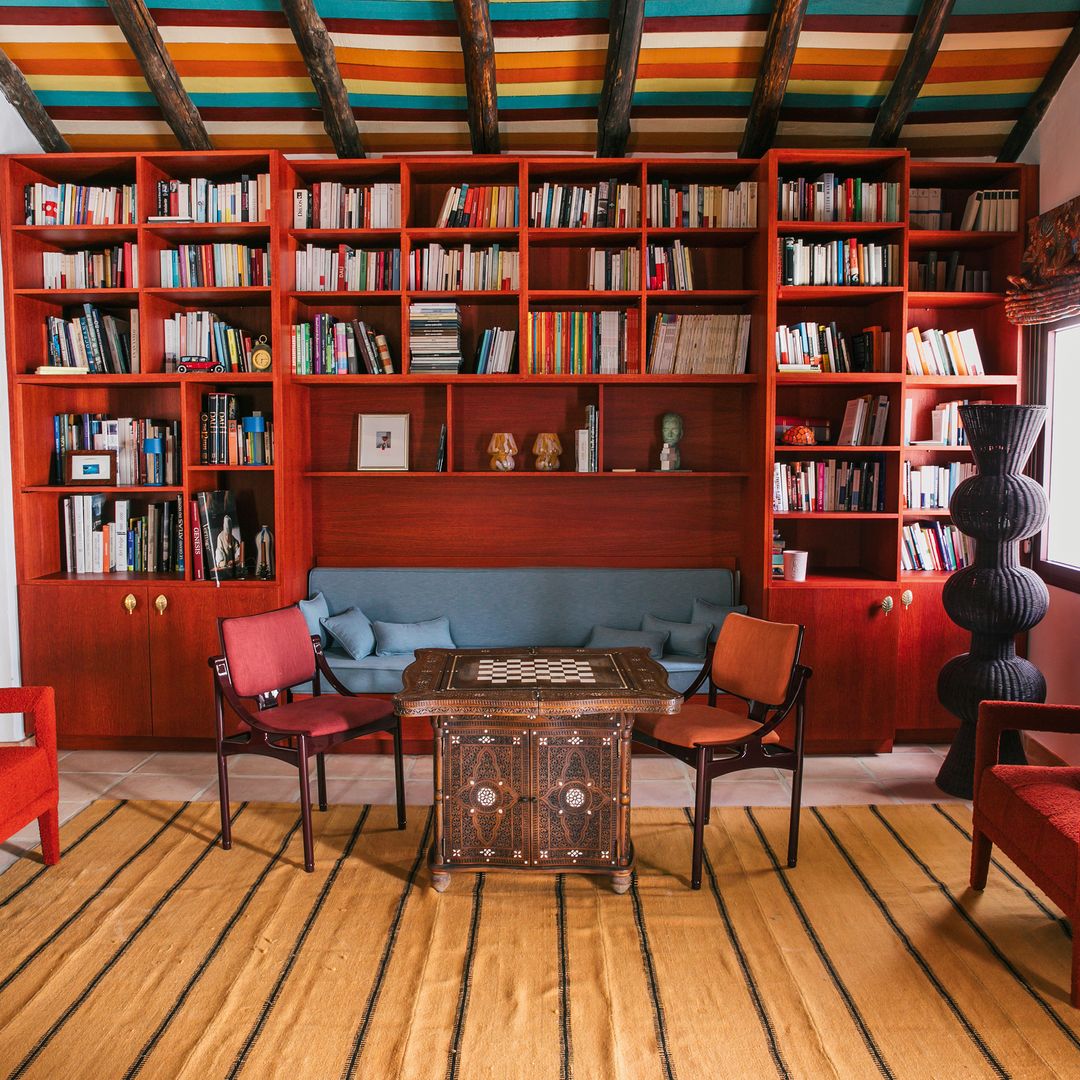 Biblioteca roja hecha a mano a medida y mesa de juego "vintage". El sofá y las butacas tienen telas Thevenon. 