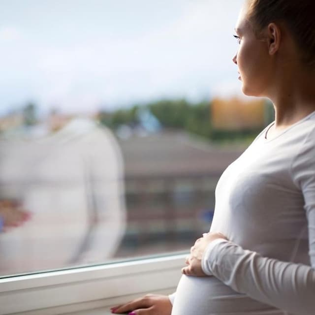 mujer embarazada pensativa mirando por la ventana