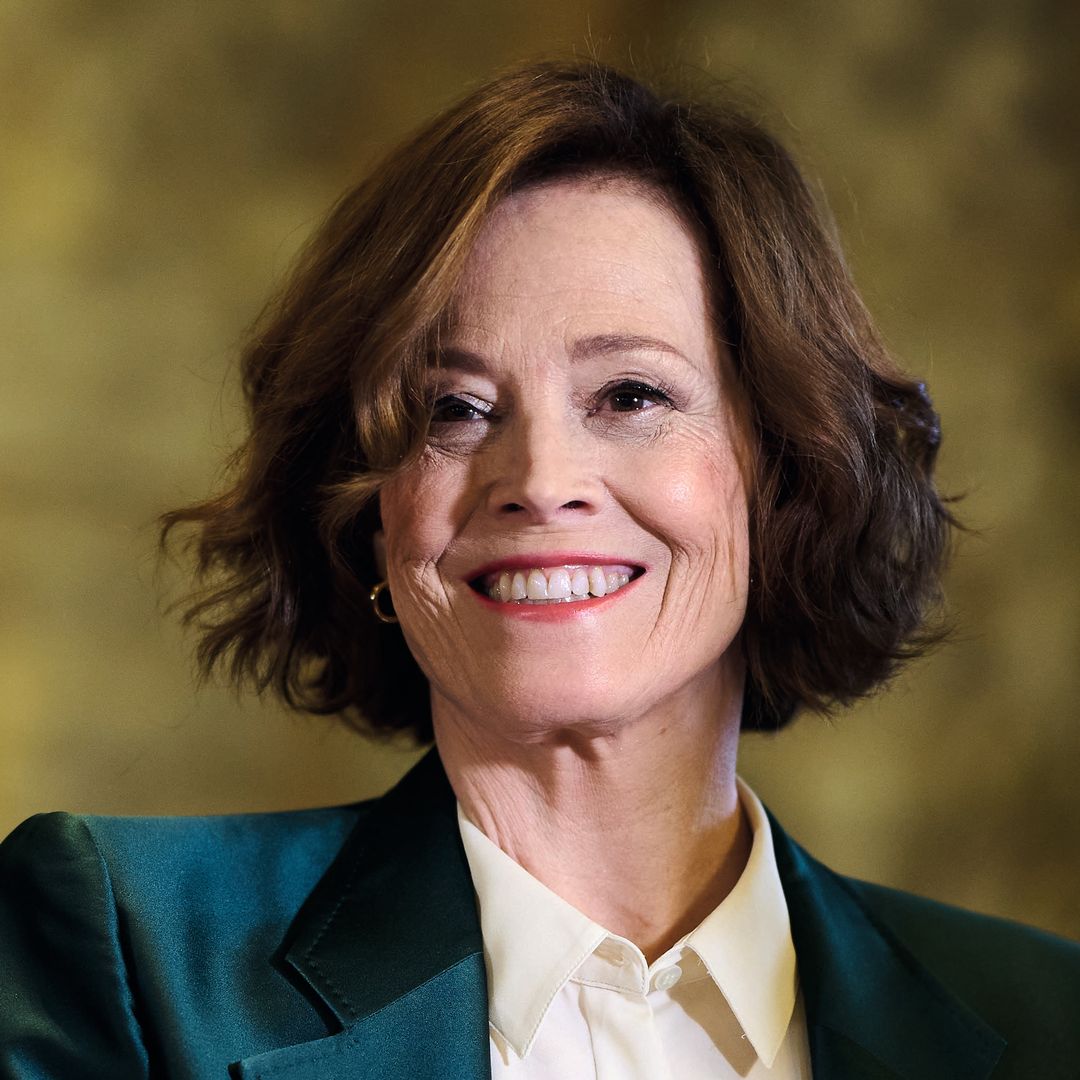 Sigourney Weaver sonríe, vistiendo un traje verde y una camisa blanca