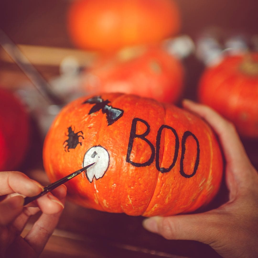 Mujer pintando una calabaza con decoración para Halloween. Primer plano de sus manos.