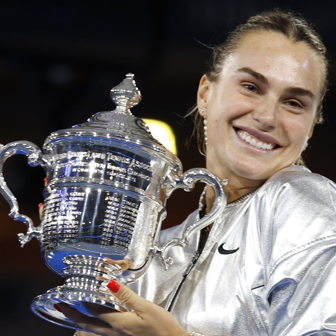 Aryna Sabalenka, sonriendo y sosteniendo un gran trofeo plateado.