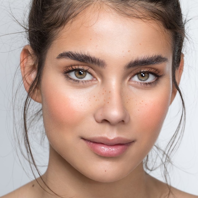 Primer plano de estudio de una hermosa adolescente de piel pecosa posando sobre un fondo gris.