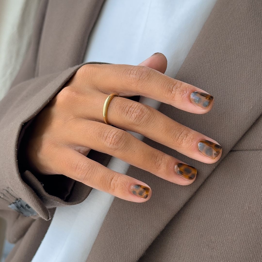 Primer plano de manicura de estampado de leopardo sobre camiseta blanca y chaqueta marrón