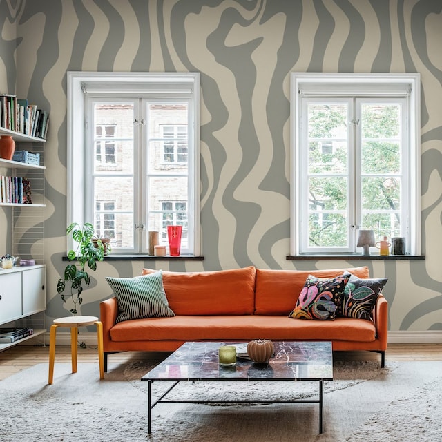 Salón con papel pintado gris con motivos geométricos, sofá naranja, mesa de centro con el sobre de mármol, alfombra y estantería