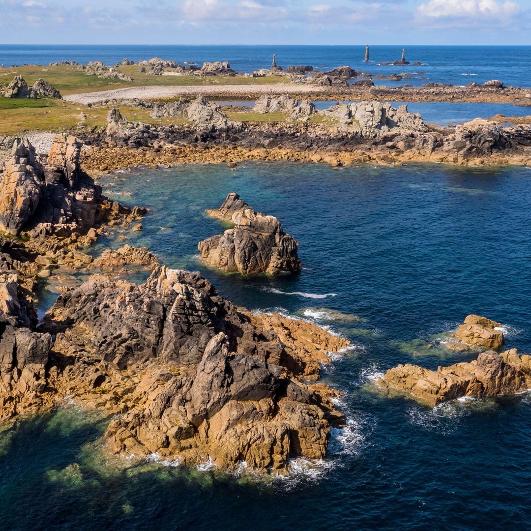 Rocas esculpidas por las tormentas al pie del faro de Créac’h, con el faro de Nividic en la punta de Pern al fondo, isla Ouessant, Bretaña, Francia