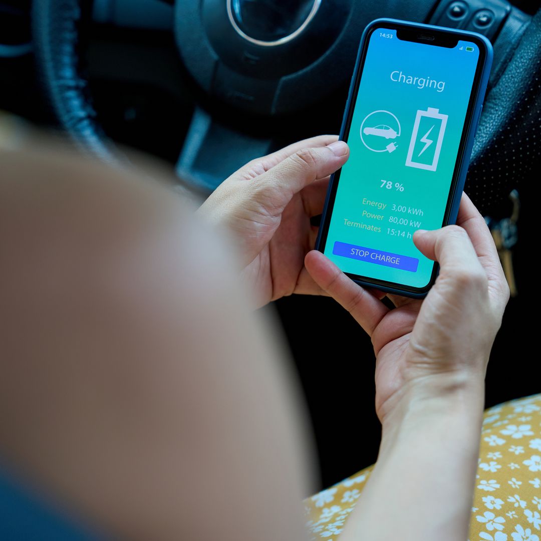 Primer plano de las manos de una mujer que utiliza una aplicación para comprobar el estado de carga de su coche eléctrico.