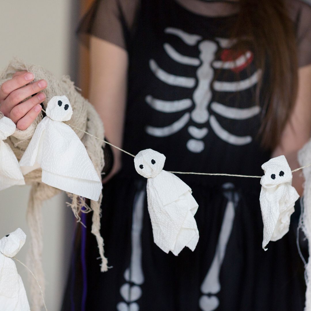 Una mujer disfrazada de Halloween mostrando una cadeneta de fantasmas casera.