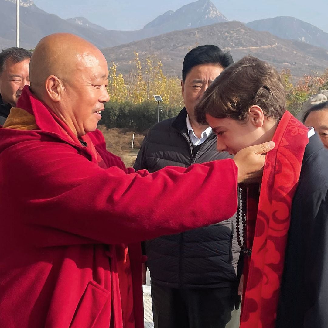 Monje en túnica roja coloca un objeto alrededor del cuello de Simeón en un acto ceremonial al aire libre
