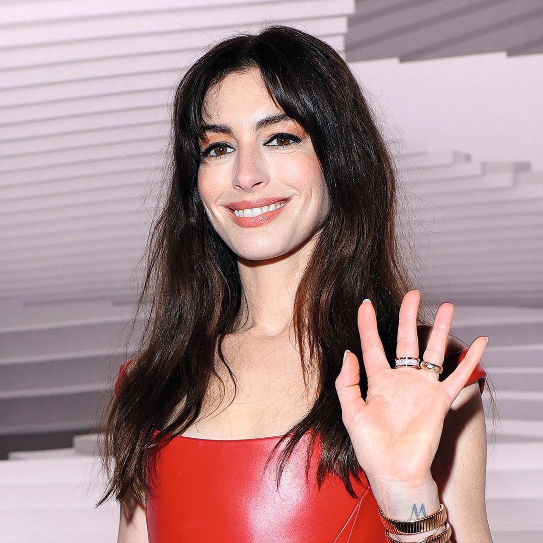 Anne Hathaway sonriendo, en un vestido rojo, posando y saludando