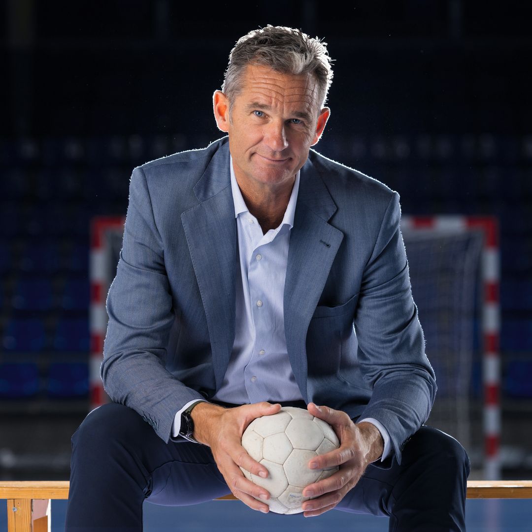 Iñaki Urdangarin en traje, sonriendo y sosteniendo un balón de fútbol en un estadio.