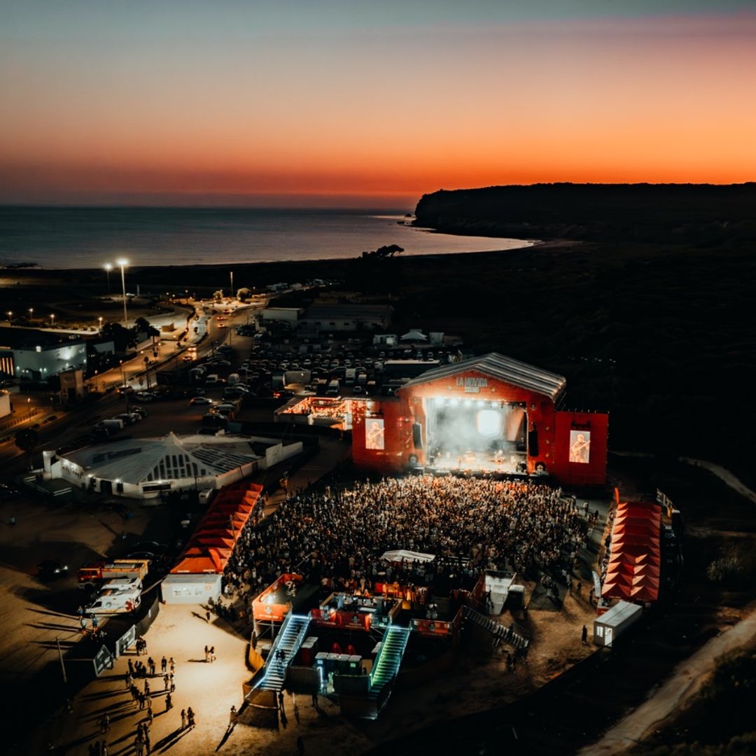 Vista aérea al atardecer de un festival junto al mar con gran multitud.