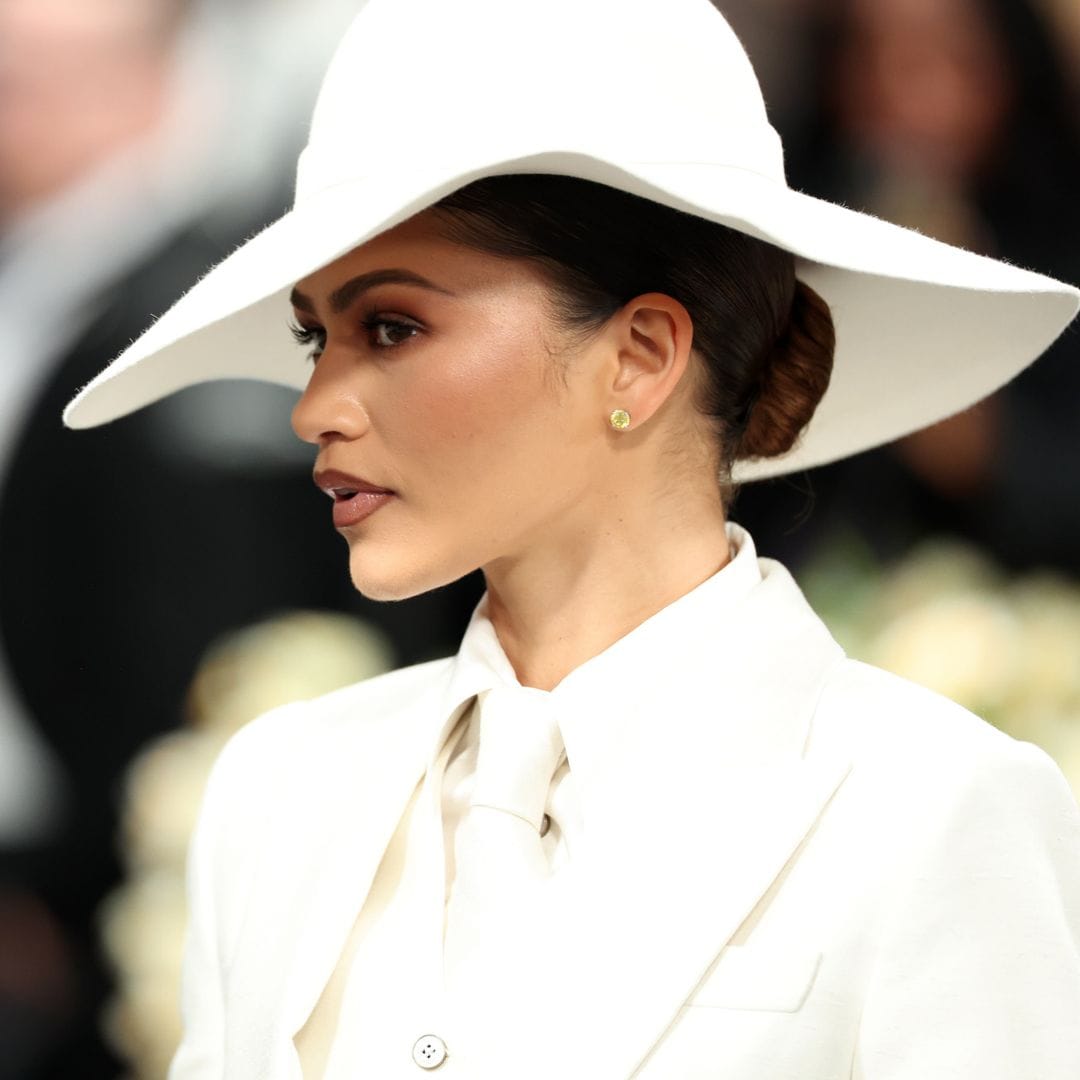 Zendaya, con traje blanco y sombrero, mira hacia un lado en un evento.