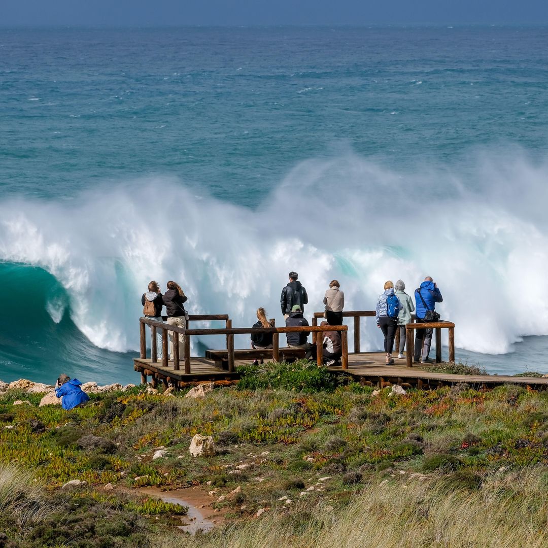 Turistas en una plataforma de observación observando el rugido del oleaje y la espuma del mar cerca de la playa do Bordeira, Carrapateira, Portugal