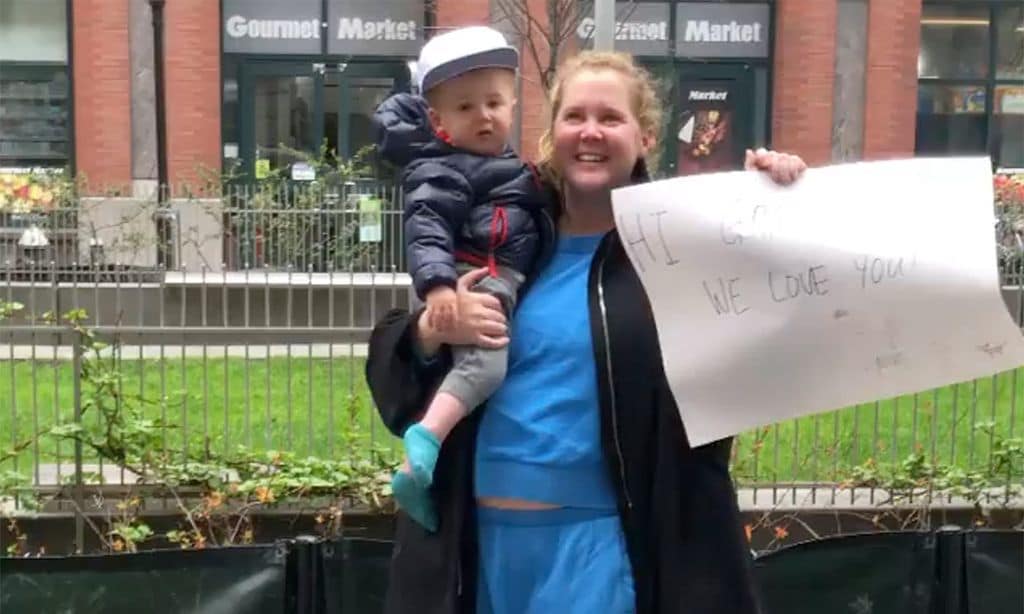 Con su hijo en un brazo y un cartel en otro, Amy Schumer envía ánimos a su padre desde la acera