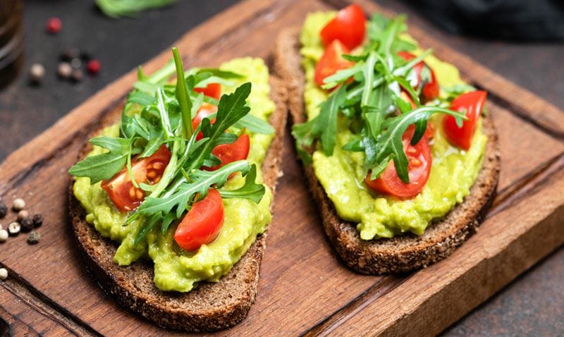 Tostadas integrales de aguacate, tomates y rúcula