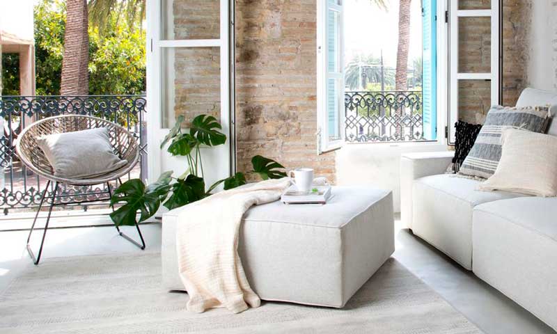 Salón con balcones decorado con un sofá y un puf en color blanco