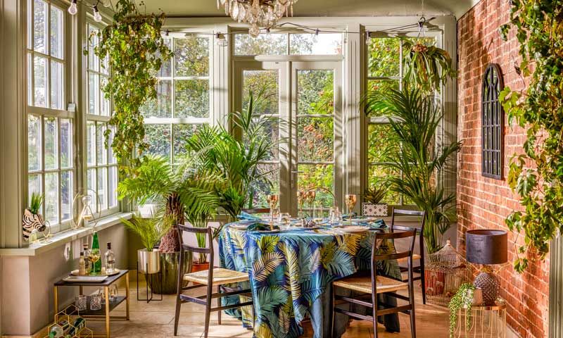 Comedor acristalado lleno de plantas exuberantes, mesa redonda y mantel tropical