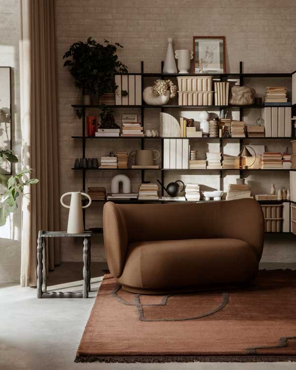Rincón del salón con sofá dos plazas curvo y en color marrón y librería de madera 