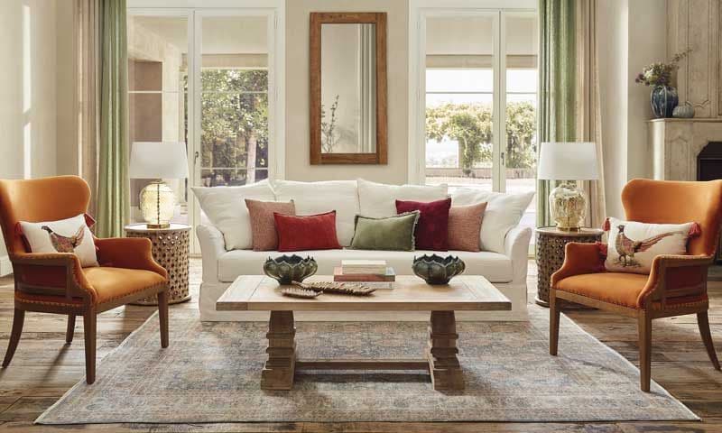 Salón clásico con chimenea, sofá blanco, butacas naranjas y cortinas verdes