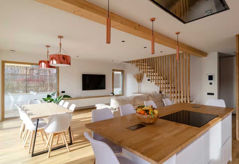 Cocina abierta al salón comedor con vigas en el techo y muebles que combinan madera blanca y clara